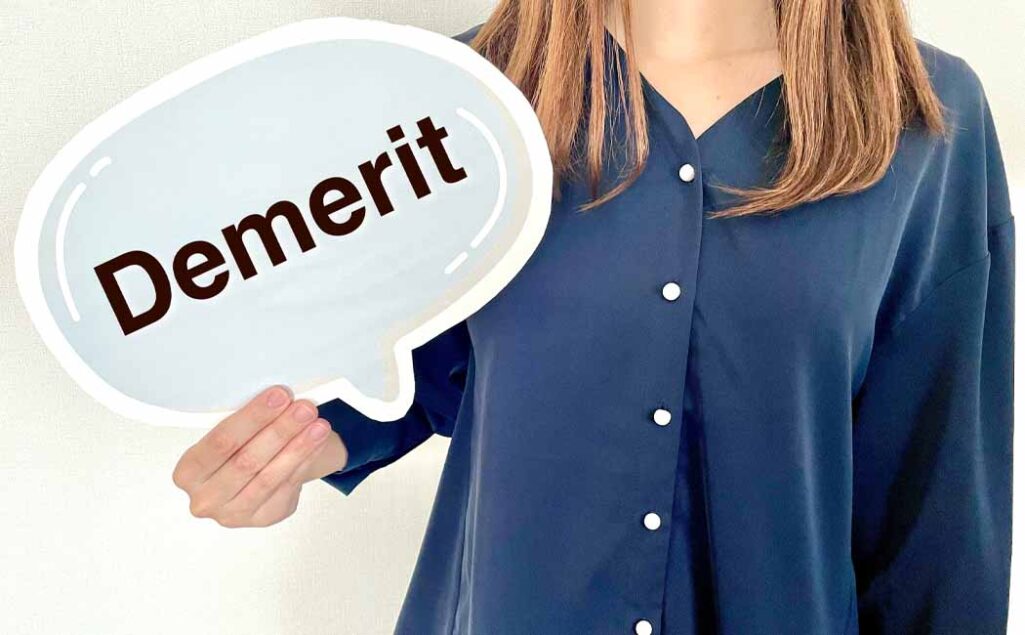 Demeritと書かれたプレートを持つ女性